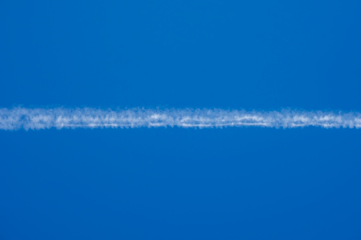 White condensation trail from an airplane flying at high altitude in a blue clear cloudless sky. Trace of water vapor and ice crystals.