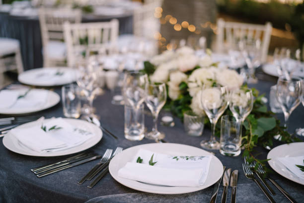 istock Wedding dinner table reception. White round plates on a round table with gray tablecloth, white Chiavari chairs with white pillows. A floral arrangement in the center of the table. 1223282041
