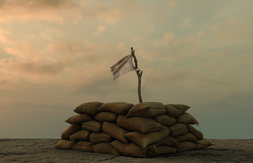 white flag behind military sand bags against sullen sky