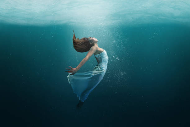 Dancer underwater in a state of peaceful levitation Elegant girl dancer in white dress in a state of levitation under the deep waters of the ocean with sunlight beaming on her face. diving into water photos stock pictures, royalty-free photos & images