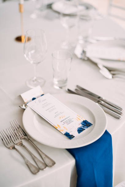 Wedding dinner table reception. White plate on the table, three forks on the left, three knives on the right. The wedding menu is in the plate. Top view