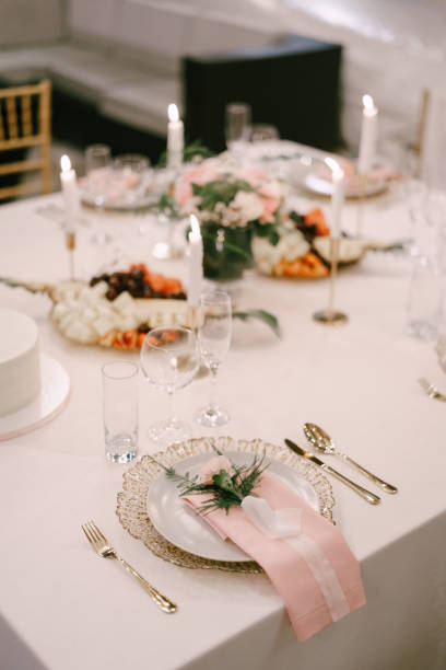 Wedding dinner table reception. Gold plate under white, pink fabric towel, pink flower with silk ribbon on top. Cutlery next to the plate. Top view