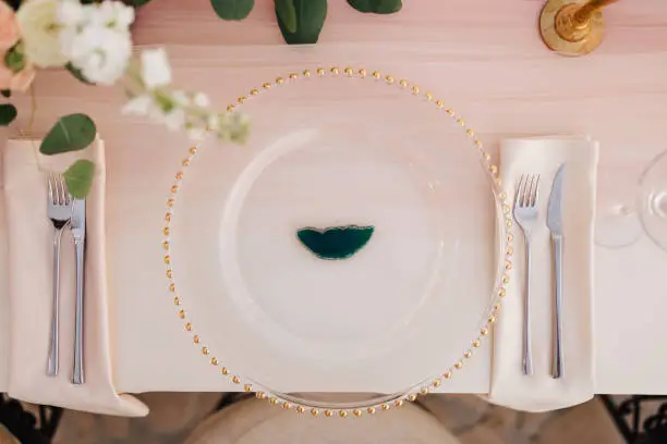 Close-up of wildcard with gold beads, transparent glass. Runner of pink silk. Candles in golden candlesticks and flowers in the center of the table.