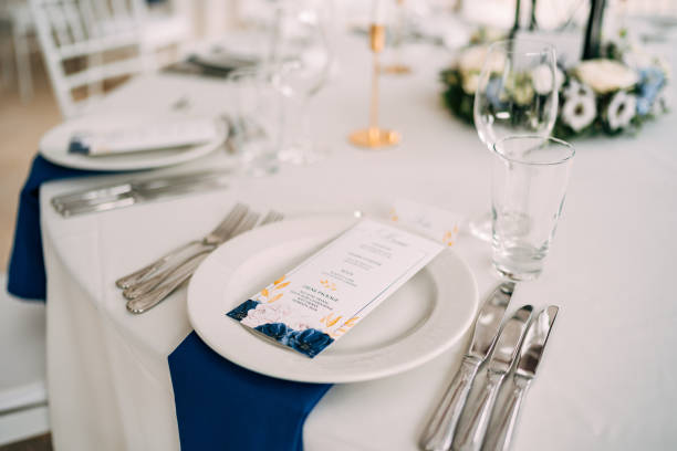 istock Wedding dinner table reception. White plate on the table, three forks on the left, three knives on the right. The wedding menu is in the plate. Top view 1223286486