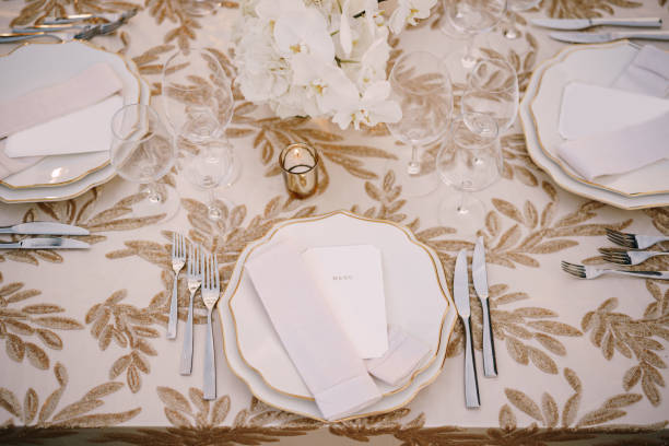 istock Wedding dinner table reception. Delicate creamy pastel tones of tablecloths and plates on table, three forks left and two knives on right, glasses and candles in candlesticks 1223286537