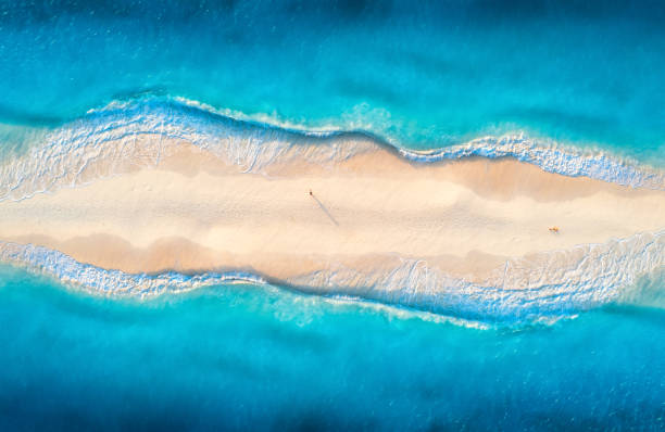 widok z lotu ptaka przejrzystego błękitnego morza z falami po obu stronach i ludzi na piaszczystej plaży o zachodzie słońca. letnia podróż w zanzibarze, afryka. tropikalny krajobraz z laguną, białym piaskiem i oceanem. widok z góry - zanzibar zdjęcia i obrazy z banku zdjęć