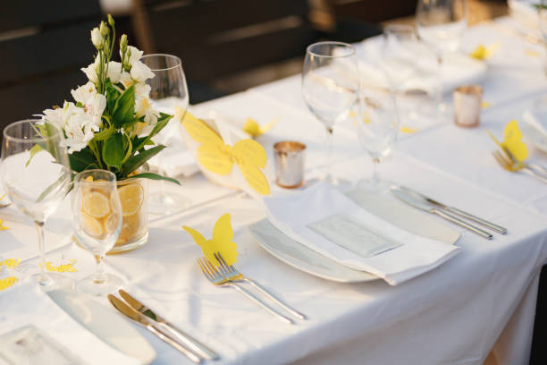 Wedding dinner table reception. Glass transparent bath with sliced lemons and a bouquet of white Alstromeri, on the table against the background of the glare of water in the sunset light