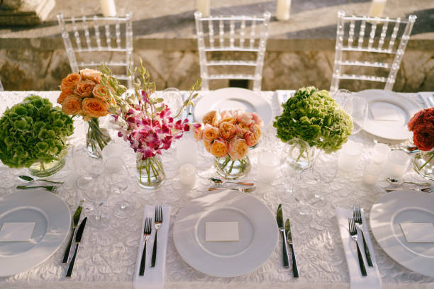 istock Wedding dinner table reception. View from above on white round plates close-up. Bouquets of pink, orange, green flowers. Pink roses, small orange roses. Top view 1223288702