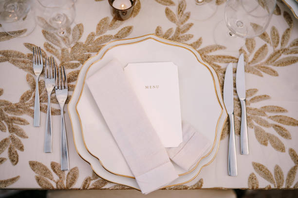 Wedding dinner table reception. Delicate creamy pastel tones of tablecloths and plates on table, three forks left and two knives on right, glasses and candles in candlesticks