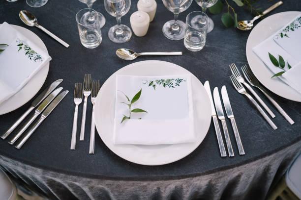 istock Wedding dinner table reception. White round plates on a round table with gray tablecloth, white Chiavari chairs with white pillows. A floral arrangement in the center of the table. 1223291619