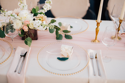 Close-up of wildcard with gold beads, transparent glass. Runner of pink silk. Candles in golden candlesticks and flowers in the center of the table.