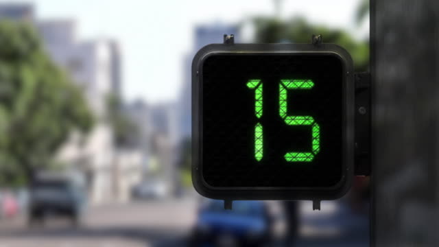 Medium shot of Walk Signal with a Green display as it shows a 15 second countdown with traffic in the background
