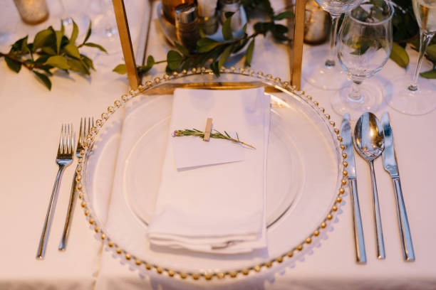 istock Wedding dinner table reception. Transparent glass plate with gold beads, on a white tablecloth, next to the cutlery. 1223293603