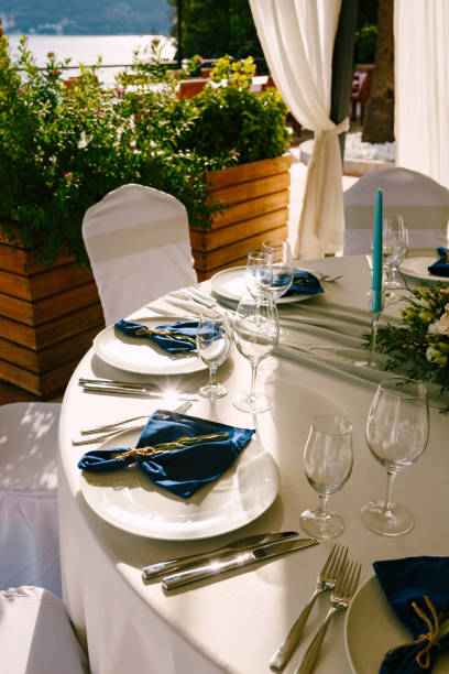 istock Wedding dinner table reception. White plates with blue cloth napkins. Glass glasses, blue candles, floral arrangement in the center of the table. 1223294274