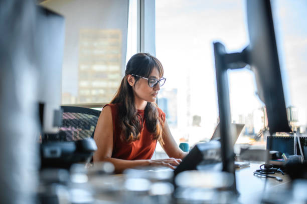 Mid Adult Buenos Aires Businesswoman Working on Laptop Low angel personal perspective of focused brunette businesswoman in mid 30s working on laptop at desk with view of downtown Buenos Aires. serious business stock pictures, royalty-free photos & images