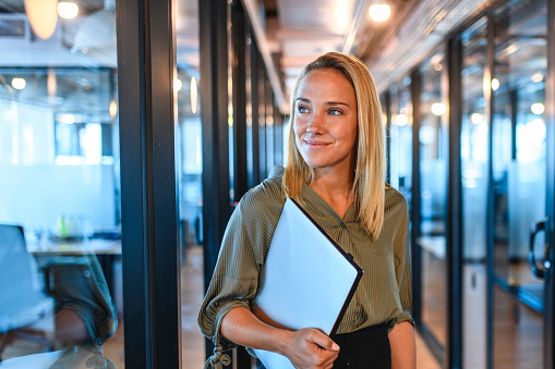Young Businesswoman Standing in Office Hallway with Laptop