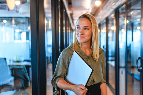 young businesswoman standing in office hallway with laptop - vanishing point imagens e fotografias de stock