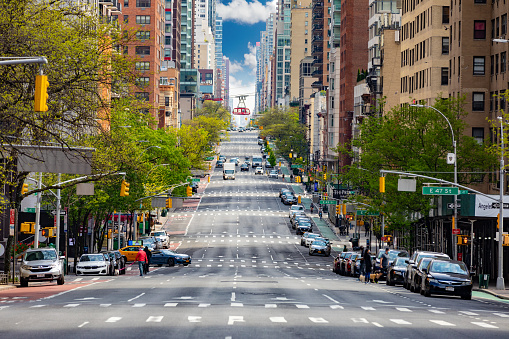 Manhattan, New York, USA - May 3, 2020: Street view looking up town 2nd Avenue with very little Traffic and Roosevelt Island Tram in background.