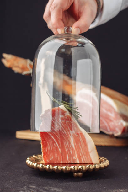 The chef opens a glass cover of meat and rosemary. Traditional spanish jamon under a glass dome on the background jamon serrano, italian parma, hamon iberico, prosciutto, leg hamon stock photo