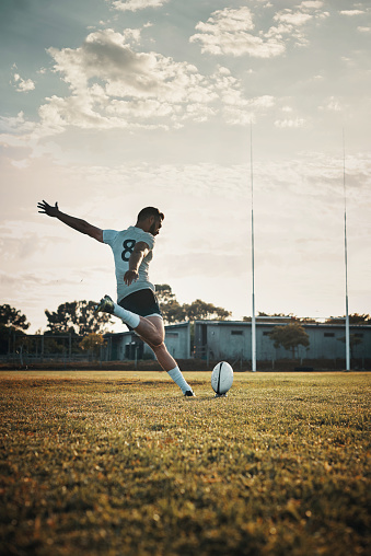Full length shot of a handsome young rugby player kicking a ball on the field during the day