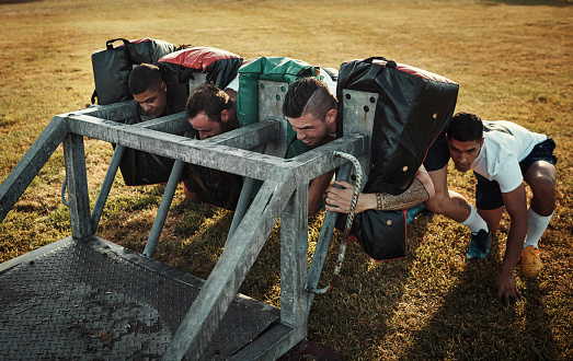 Full length shot of a group of young rugby players training with tackle bags on the field during the day