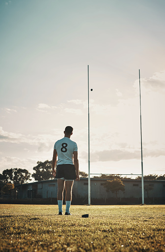 Rearview shot of a handsome young rugby player kick  training on the field during the day