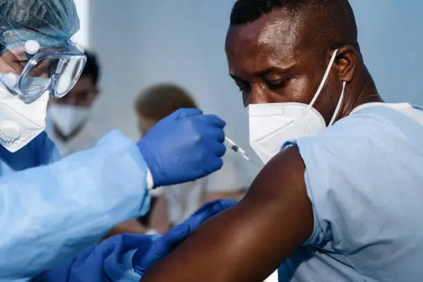 african americam man looking at coronavirus covid-19 syring when medical staff injecting vaccine to arm muscle to build immunization of coronavirus covid-19 for him