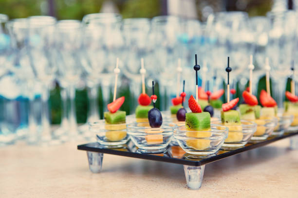 verschiedene kanapees von obst und käse auf einer glasplatte auf dem hintergrund von gläsern und champagner. catering - canape buffet cocktail food stock-fotos und bilder