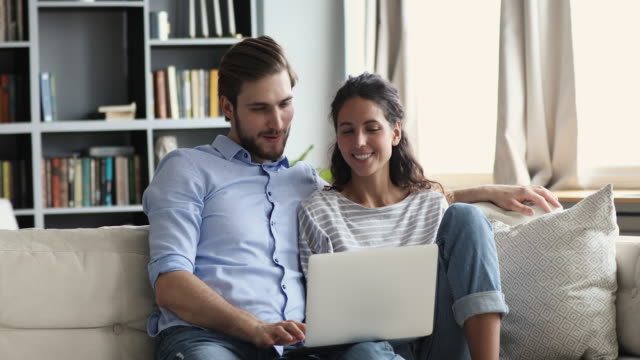 Smiling relaxed young couple using laptop at home on couch