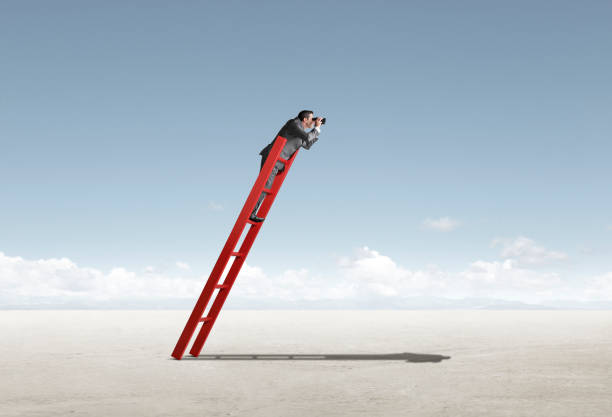 istock Businessman On Leaning Ladder Looks Through Binoculars 1223327488