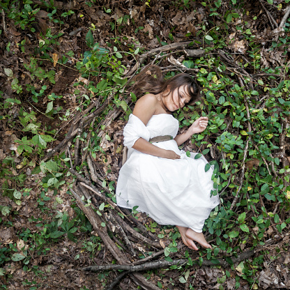 Fantasy scene of a pregnant Caucasian woman wearing a white gown lying curled up in a giant nest of grapevine, branches and leaves outdoors nesting while she waits for her baby to be born, Indiana, USA