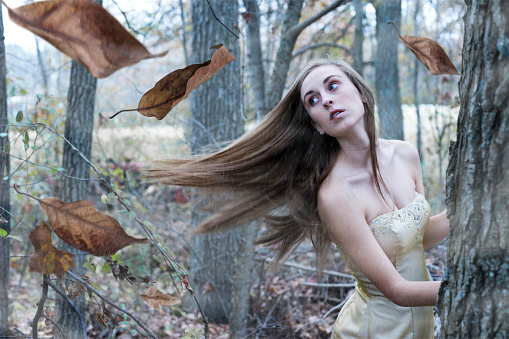 Female heroine in a gold gown flees from danger in the woods on a windy, rainy autumn day, Indiana, USA
