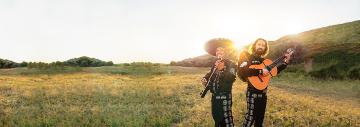 Mexican musicians mariachi on the background of field and mountains at sunset.