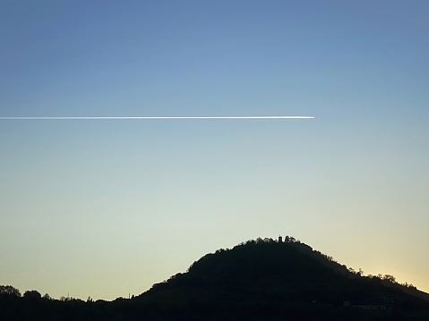 Lonely Passenger Airplane flying over Achalm Mount and Achalm Castle Ruins at Sunrise. Single Airplane Contrail over Achalm Mount, Reutlingen, Baden Württemberg, Germany