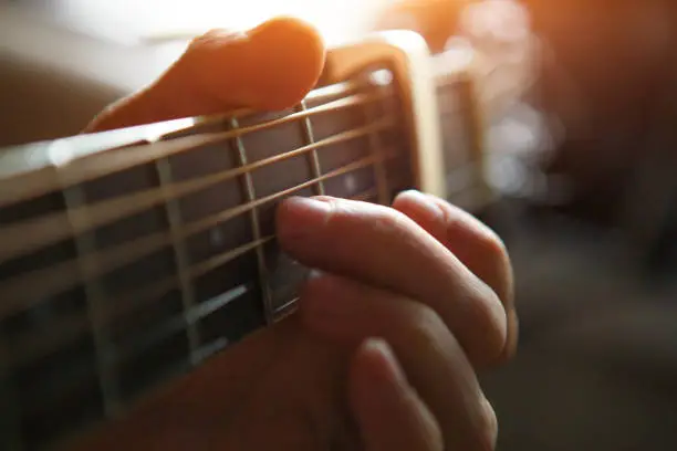 The fingers of a man's hand on the neck of a guitar clamp the strings close-up. Guitar playing, beautiful lighting, background with space for text
