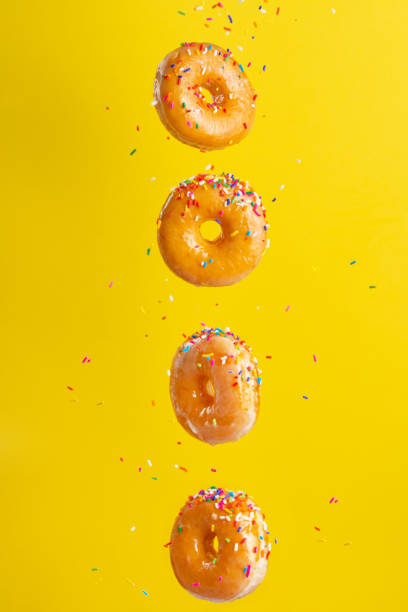 istock Flying donuts. Many donuts with colored caramel with sprinkles on a yellow background. Vertical photo. Freezing in motion. 1223341443