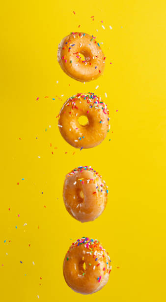 istock Various decorated donuts in motion falling on a yellow background. Sweet and iced donuts fall or fly in motion. With caramel. Yellow background, vertical photo. 1223341617
