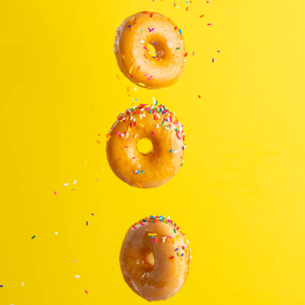 istock Flying donuts. Many donuts with colored caramel with sprinkles on a yellow background. Vertical photo. Freezing in motion. 1223341854