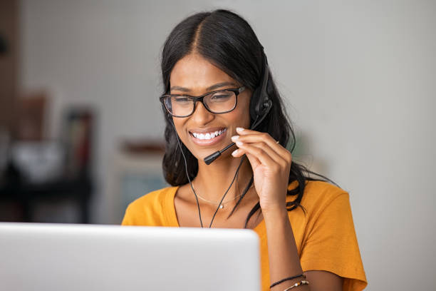 Happy indian woman working in a call center Portrait of cheerful indian woman in smart working from home. Beautiful middle eastern girl working as customer service representative with laptop. Smiling young woman at home with headset doing video call and smiling. customer service representative photos stock pictures, royalty-free photos & images