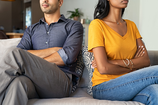 Middle eastern couple sitting back to back after a fight on the sofa. Young indian couple in fight with arms crossed sitting on couch after quarrel at home. Young mixed race woman and his boyfriend sitting next to each other angry.
