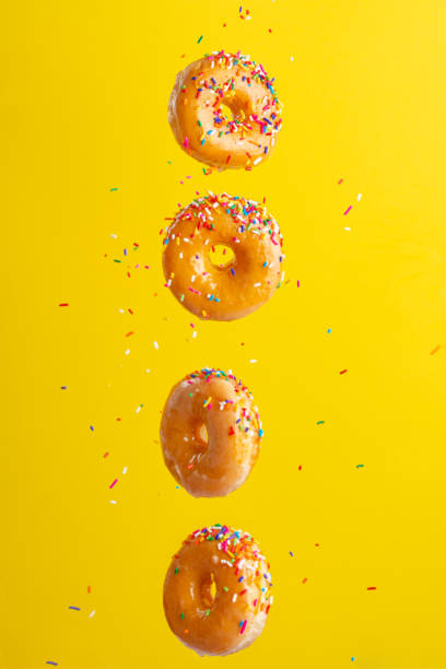 istock Flying donuts. Many donuts with colored caramel with sprinkles on a yellow background. Vertical photo. Freezing in motion. 1223344020