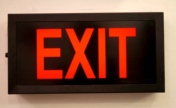 istock Close-up of electrical illuminated exit sign board on the wall 1223344397