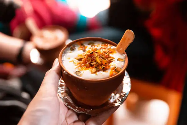 Photo of Indian popular drink lassi (traditional dahi yogurt-based drink) in clay cup with various topping on the street in Varanasi.