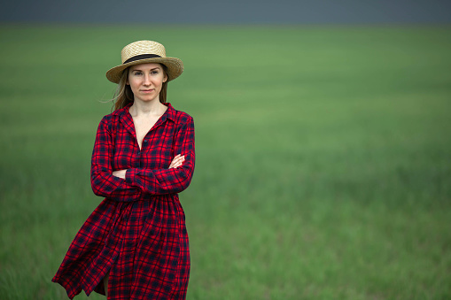 Portrait of a young woman farmer standing on fertile agricultural soil of farm land, looking into the distance.