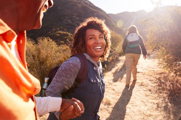 donna che aiuta l'uomo sul sentiero come gruppo di amici anziani andare a piedi in campagna insieme - active holidays foto e immagini stock