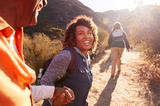 シニアフレンズのグループとしてトレイルで男を助ける女性は一緒に田舎でハイキングに行く - ハイキング ストックフォトと画像