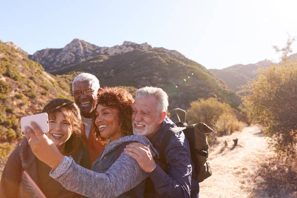 group of senior friends posing for selfie as they hike along trail in countryside together - photography friendship vacations horizontal imagens e fotografias de stock