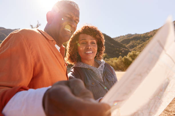 senior couple looking at map as they hike along trail in countryside together - senior adult mountain hiking recreational pursuit imagens e fotografias de stock