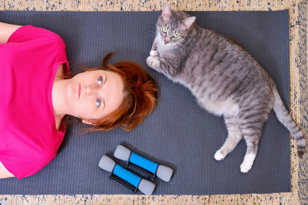 A tired woman and a cat lie on a training mat after a sports workout. Concept of isolation during the coronavirus epidemic and sports training A tired woman and a cat lie on a training mat after a sports workout. Concept of isolation during the coronavirus epidemic and sports training woman lying on the floor isolated stock pictures, royalty-free photos & images