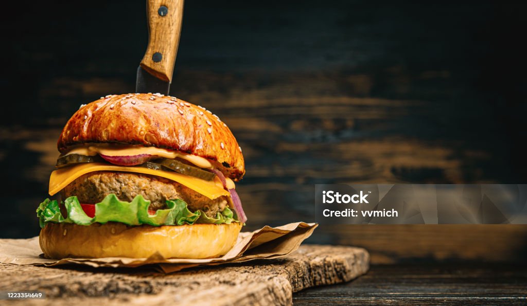 close up tasty beef burger close up tasty beef burger on a wooden table with a knife inserted into it Cheeseburger Stock Photo
